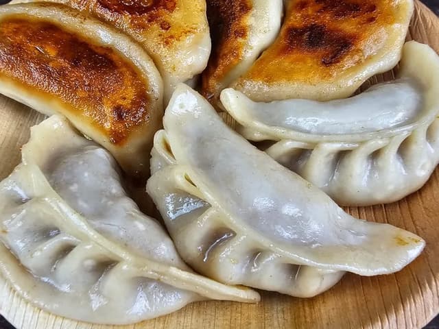 Pan-seared gyoza arranged on a wooden plate.